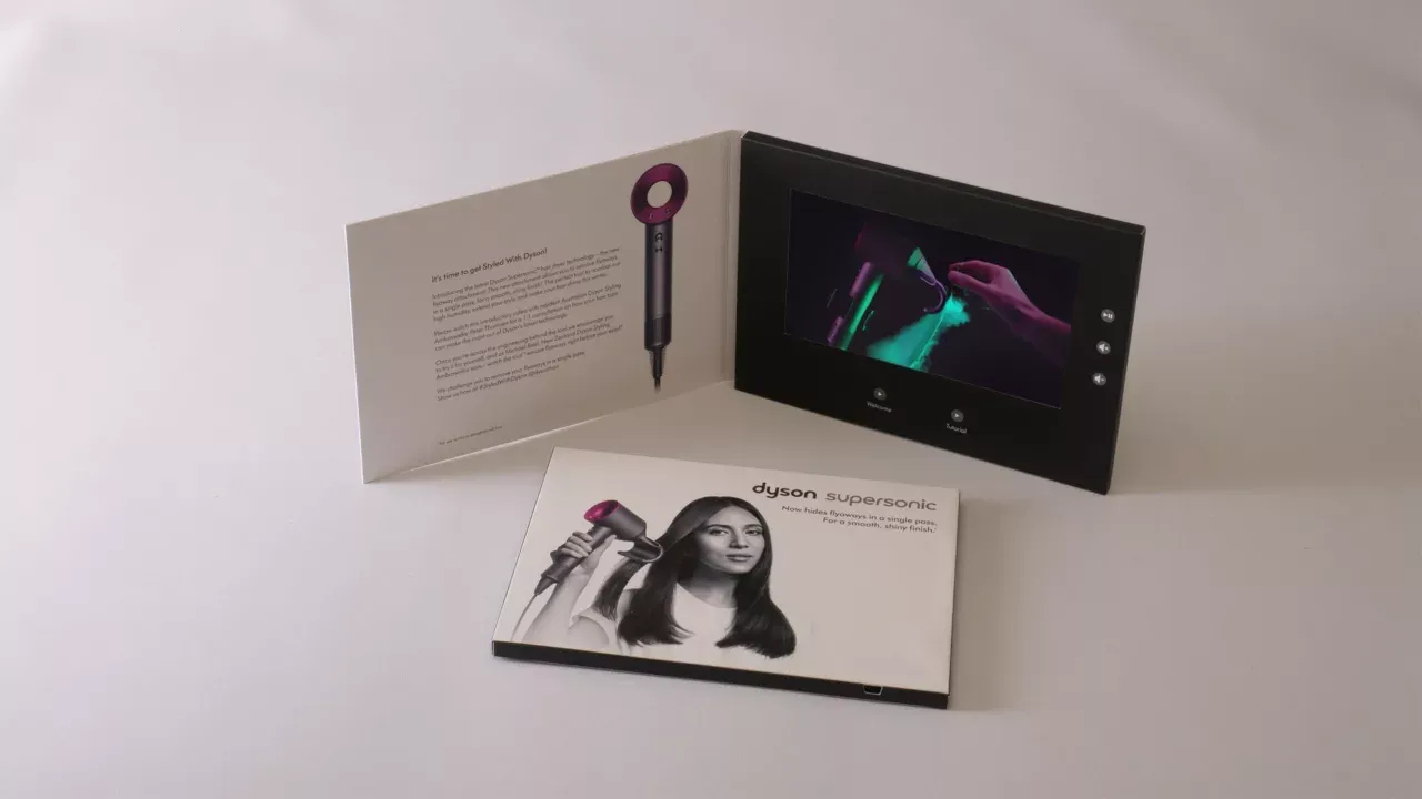An open MediaTech videobook for the Dyson Supersonic: a hardcover with an embedded screen playing a product video, shown beside its printed insert and a second closed copy.